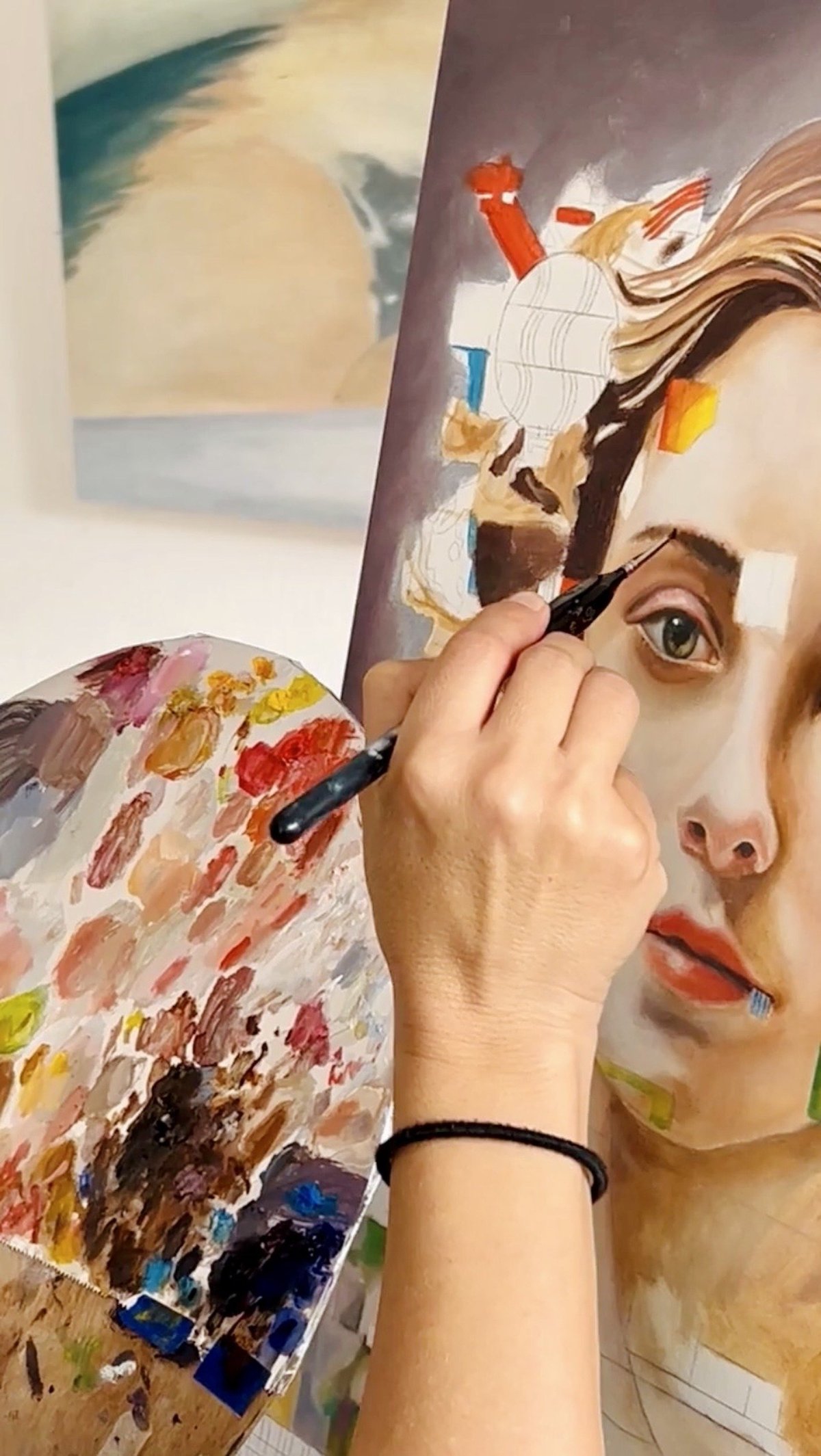 Artists hand painting a portrait of a womans face with a brush, palette visible below
