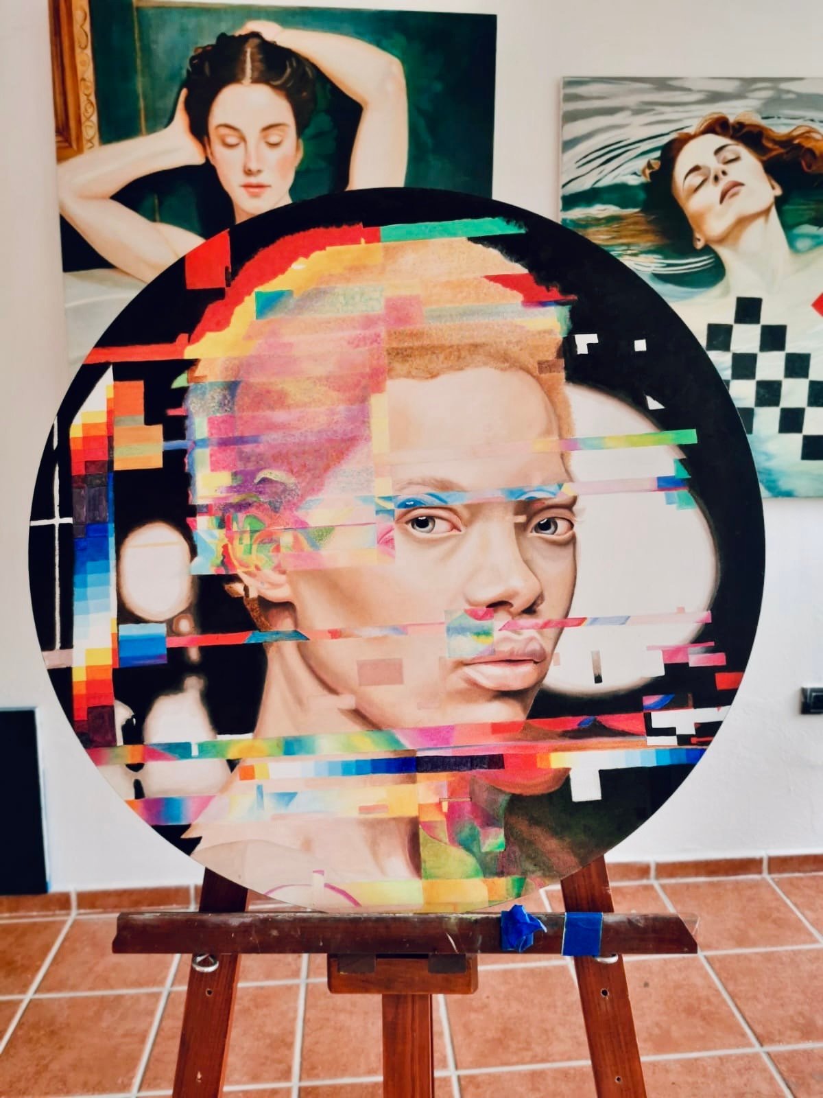 Circular portrait artwork with pixelated, colorful digital glitch effect overlaying a mans face on wooden easel